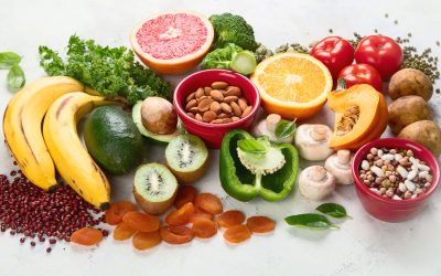 A spread of healthy foods high in potassium, including bananas, avocado, potatoes, dried apricots, beans, oranges, and assorted vegetables