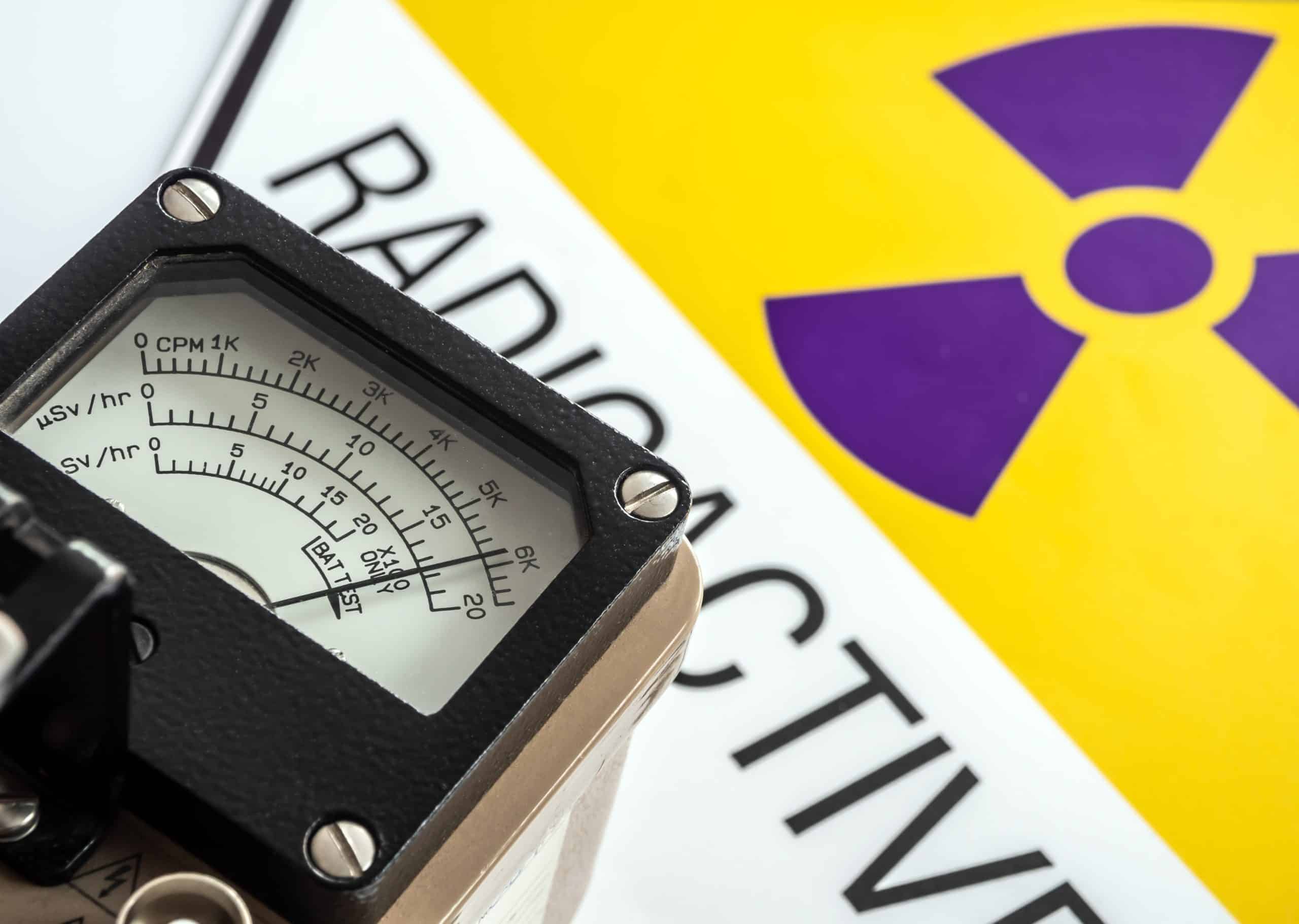 Dose rate meter in front of a sign with a nuclear trefoil and the word RADIOACTIVE.