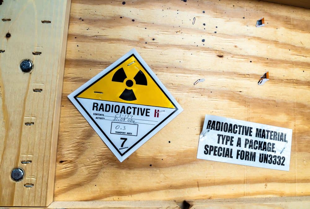 A Class 7 radioactive materials shipping label on a wooden crate, showing the yellow-and-white radiation trefoil, category II-yellow with two red bars, and handwritten contents, activity, and transport index fields; beside it a printed label reads "Radioactive Material, Type A Package, Special Form UN3332