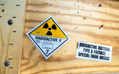 A Class 7 radioactive materials shipping label on a wooden crate, showing the yellow-and-white radiation trefoil, category II-yellow with two red bars, and handwritten contents, activity, and transport index fields; beside it a printed label reads "Radioactive Material, Type A Package, Special Form UN3332
